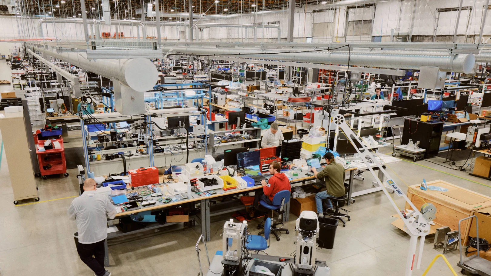 Workers assemble humanoid-robot components at benches inside an Agility Robotics production facility.