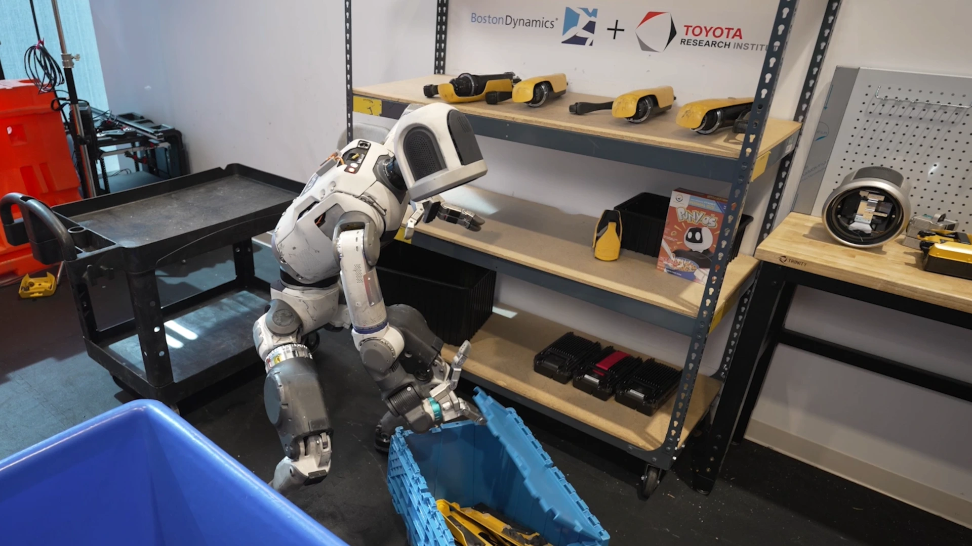 Atlas beside a blue parts crate in a research setting. August 2025 contextual photograph, not the CEO appointment or a 2026 factory deployment.