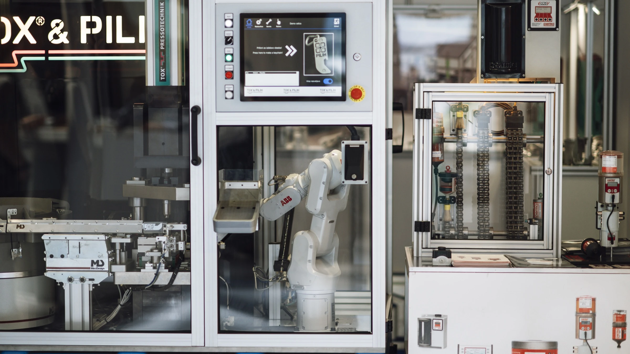 A white ABB industrial robot arm works inside a guarded factory cell beside machine tools and a control display.