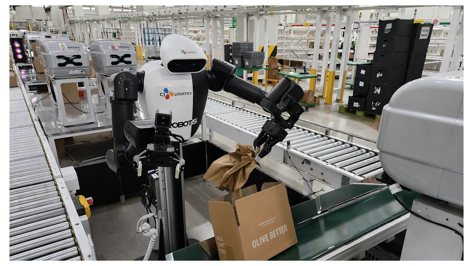 ROBOTIS humanoid inserts cushioning material into an Olive Young shipping box at a CJ Logistics center