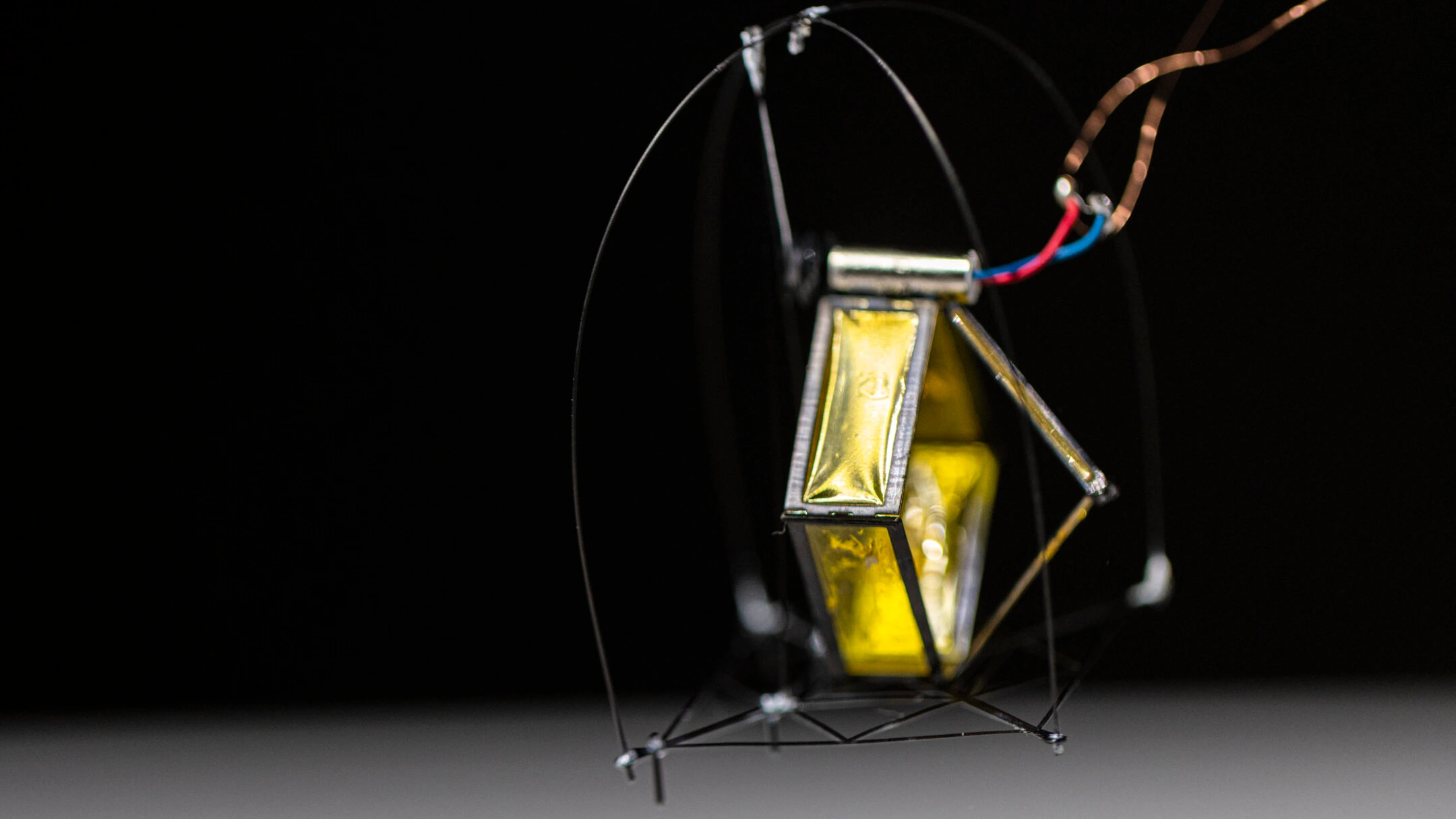 The black and gold DirectHop prototype above a tabletop, with power wires attached and a curved protective cage around its body.