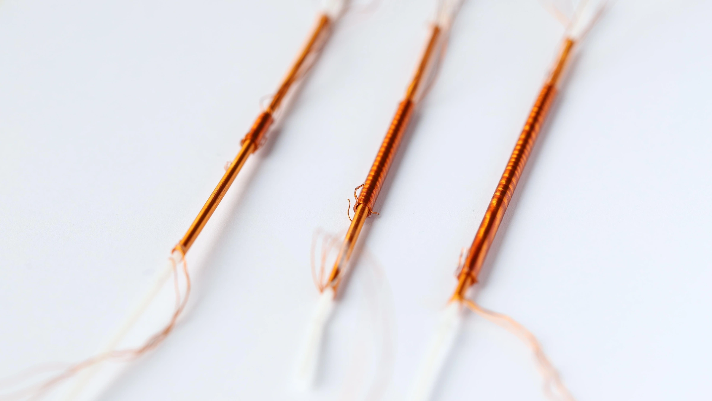 Three copper-colored EPFL FiberMotor research prototypes on a white surface. Supplied 2026 laboratory photograph, not an operating wearable product.
