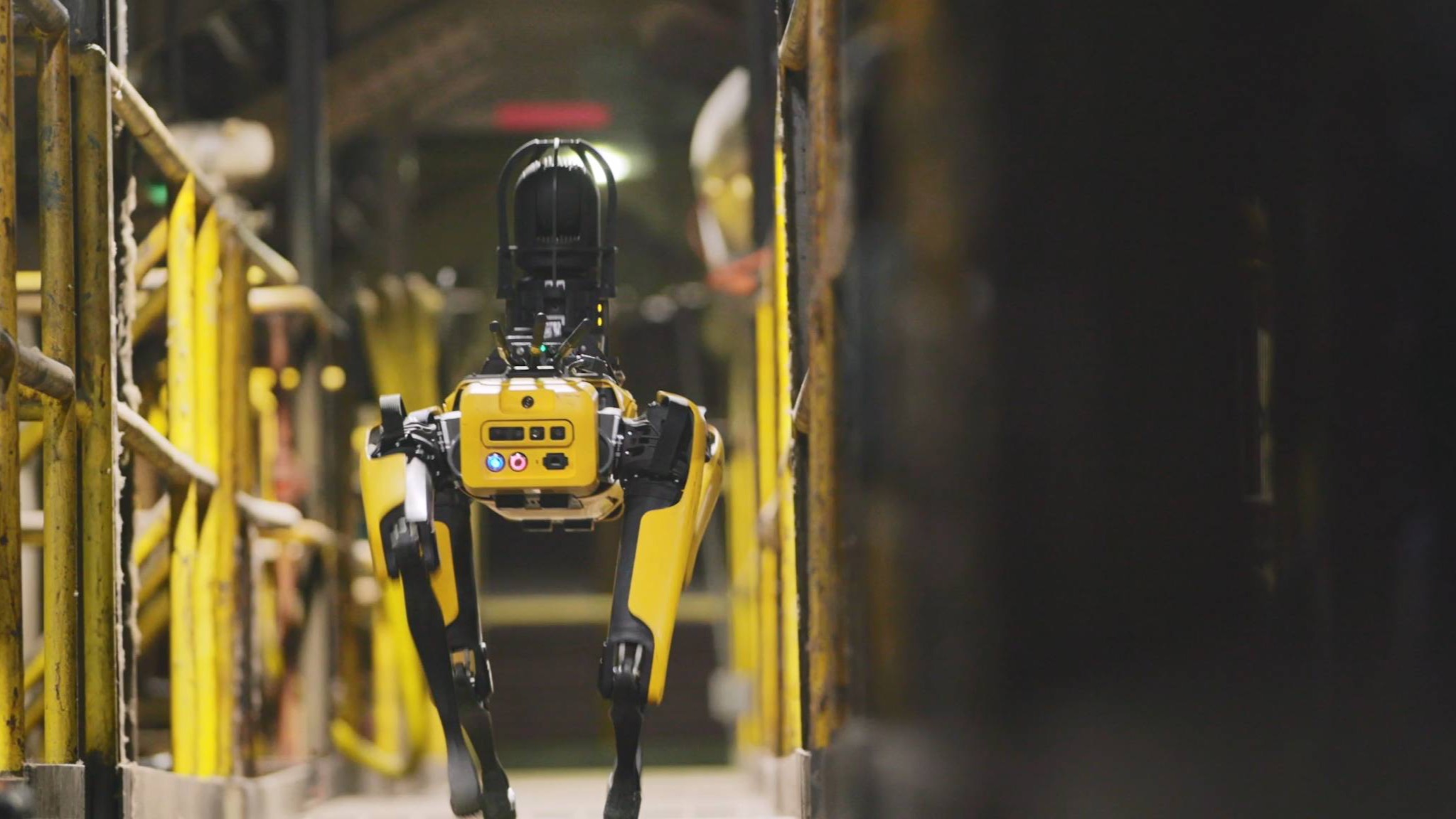 Boston Dynamics Spot walks through an industrial facility in an official product photograph.