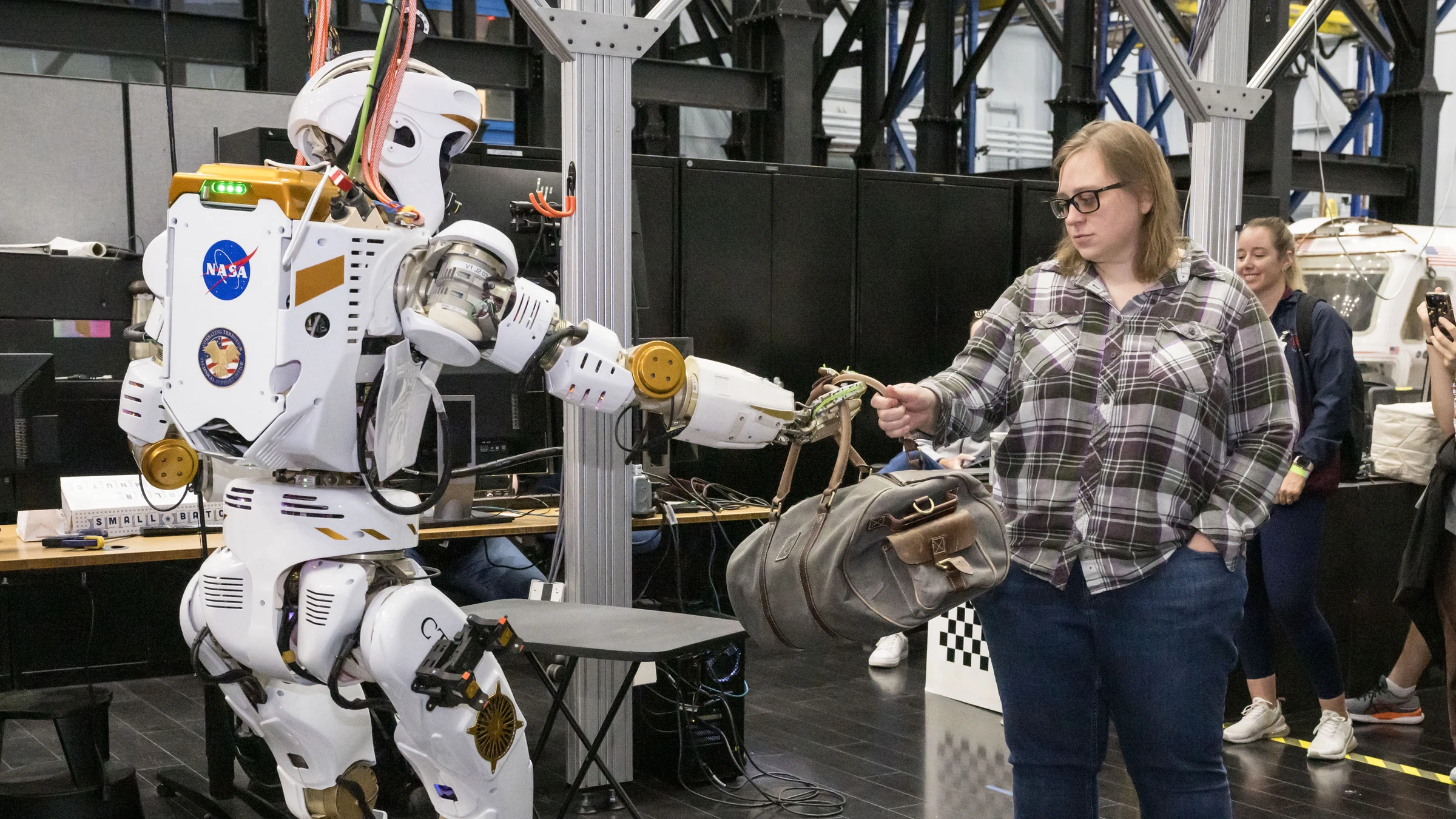 NASA’s Valkyrie humanoid hands a duffel bag to a person during a March 2024 laboratory demonstration at Johnson Space Center; an archive photograph, not the spacecraft-hatch test.