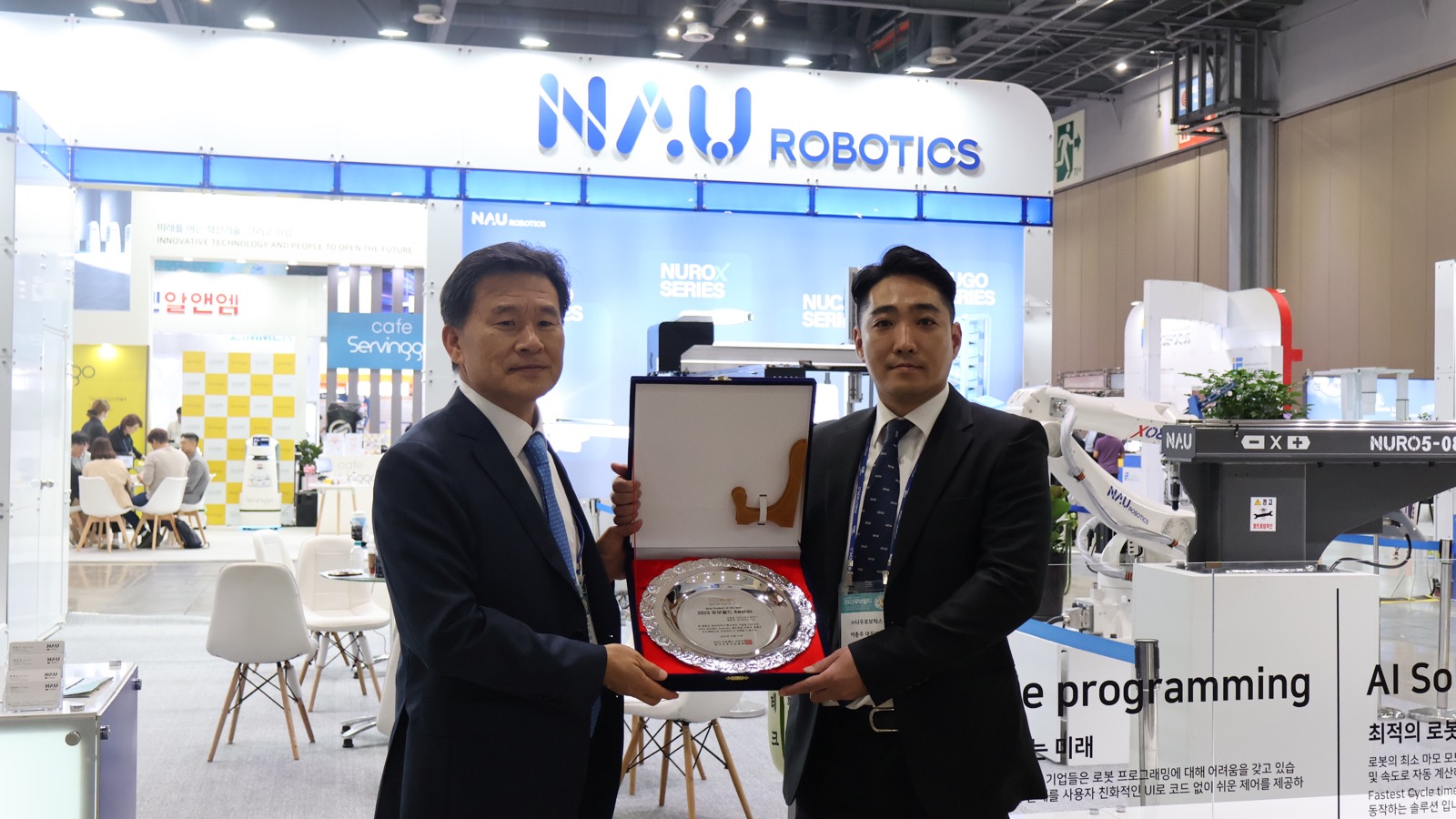 Now Robotics executives stand beside a NURO industrial robot at the company’s exhibition booth