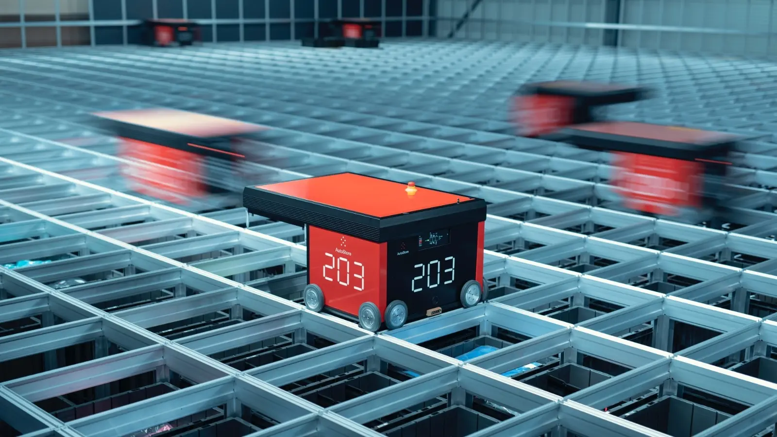 A red AutoStore robot moves across a dense warehouse grid while other robots work behind it.