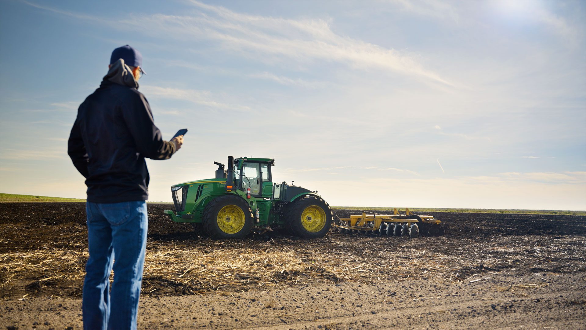 A John Deere tractor works a South Florida field while a worker monitors it from a handheld device