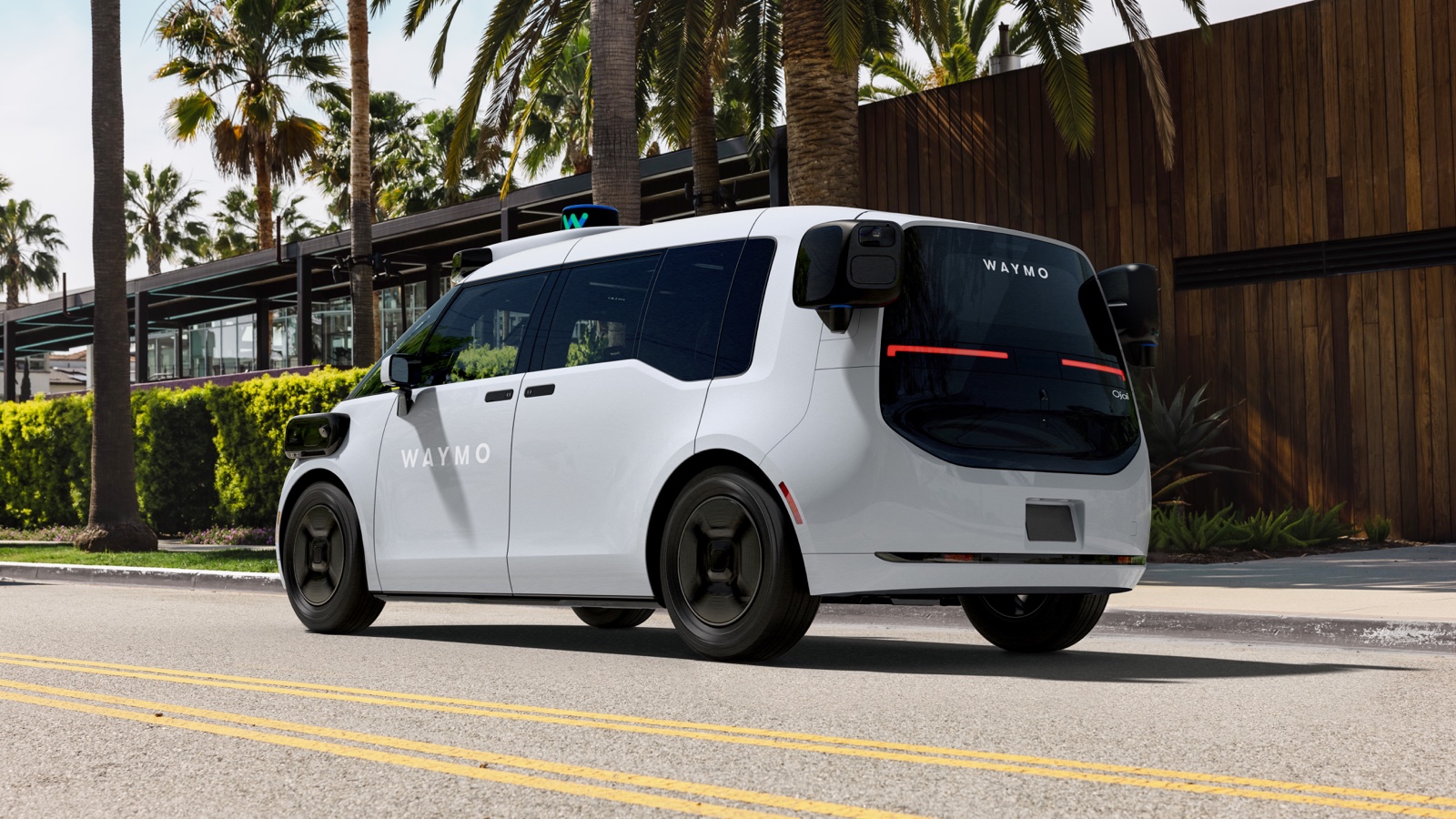Waymo's white Ojai autonomous vehicle drives on a palm-lined California street