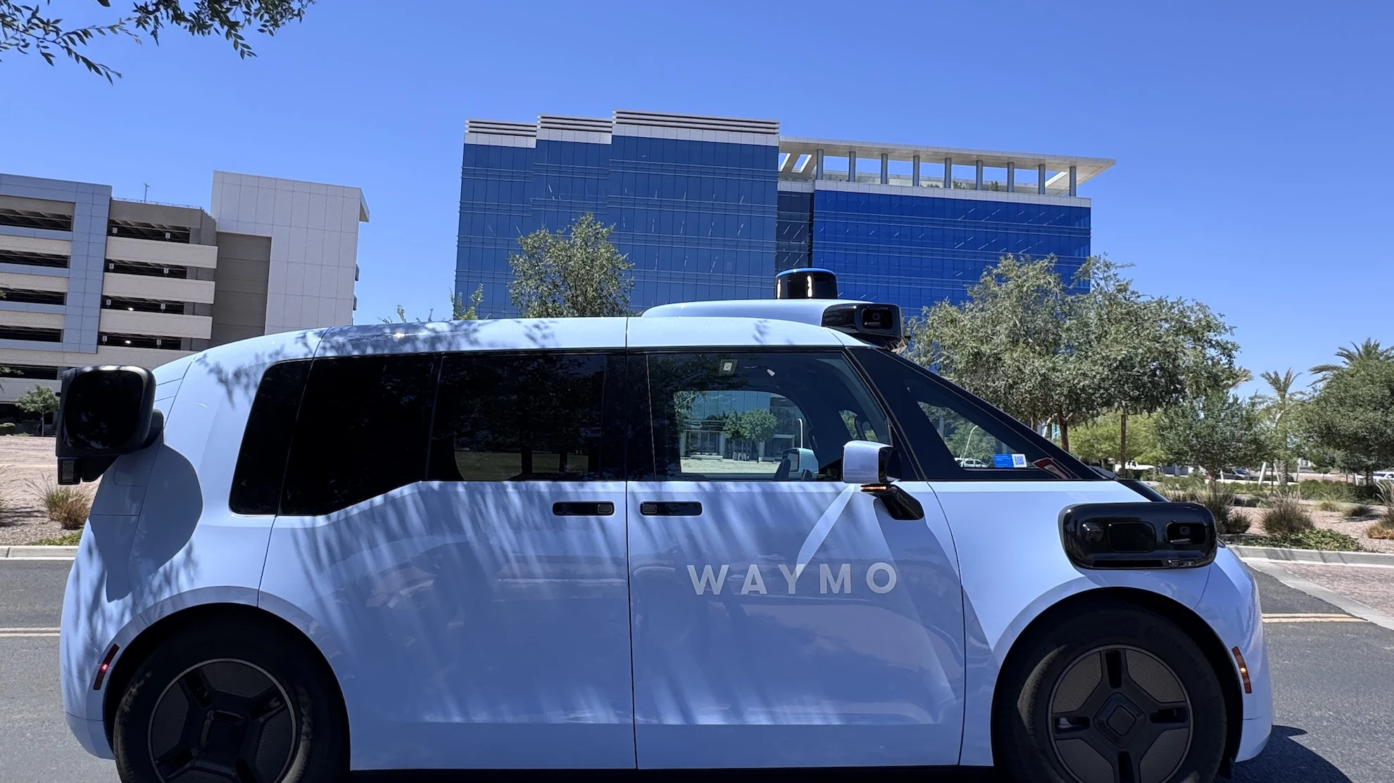 Waymo Zeekr Ojai robotaxi parked outside a glass-fronted building