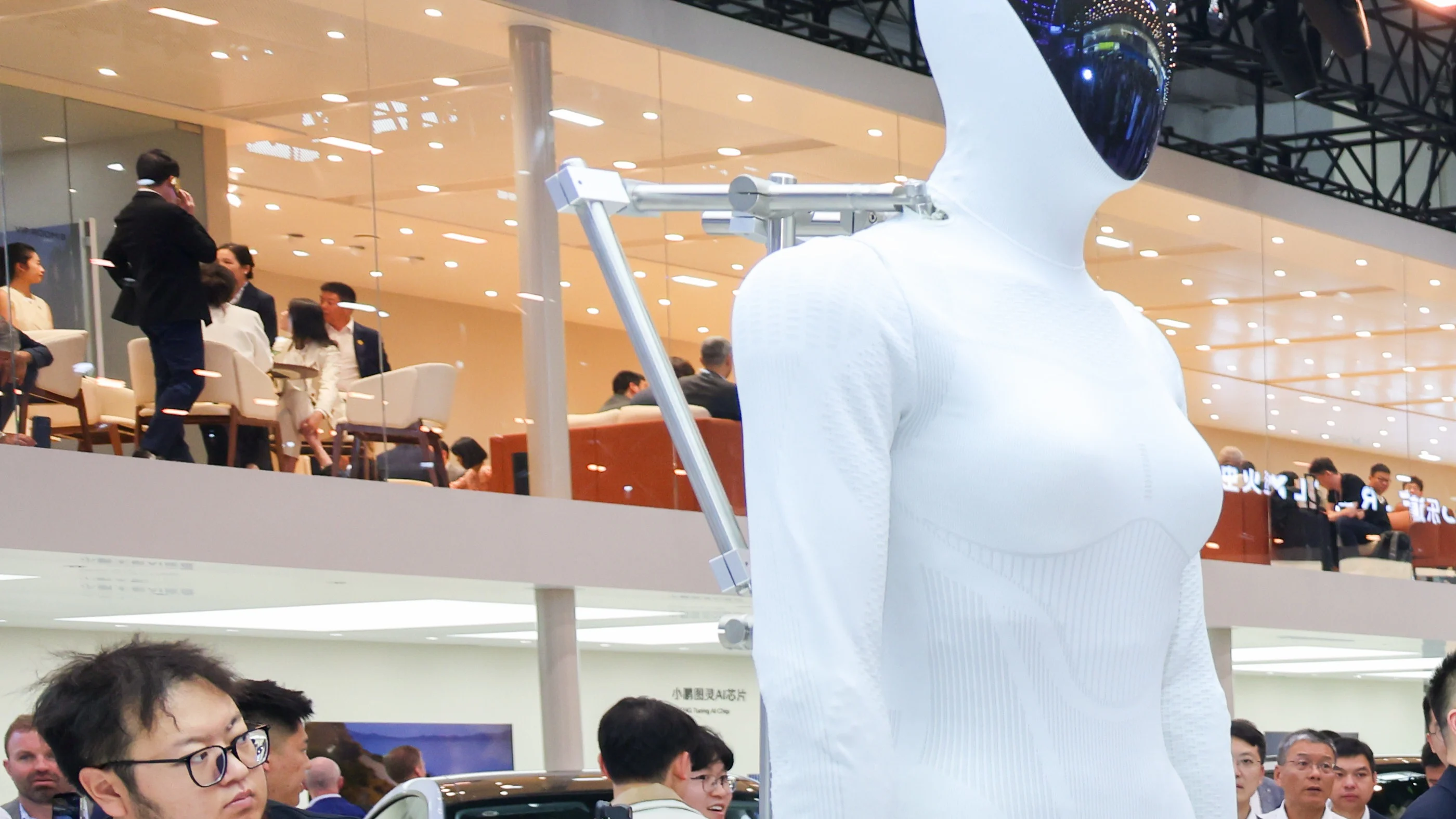 Close official photograph of an XPENG IRON humanoid at an XPENG display, with attendees and exhibition lighting behind it.